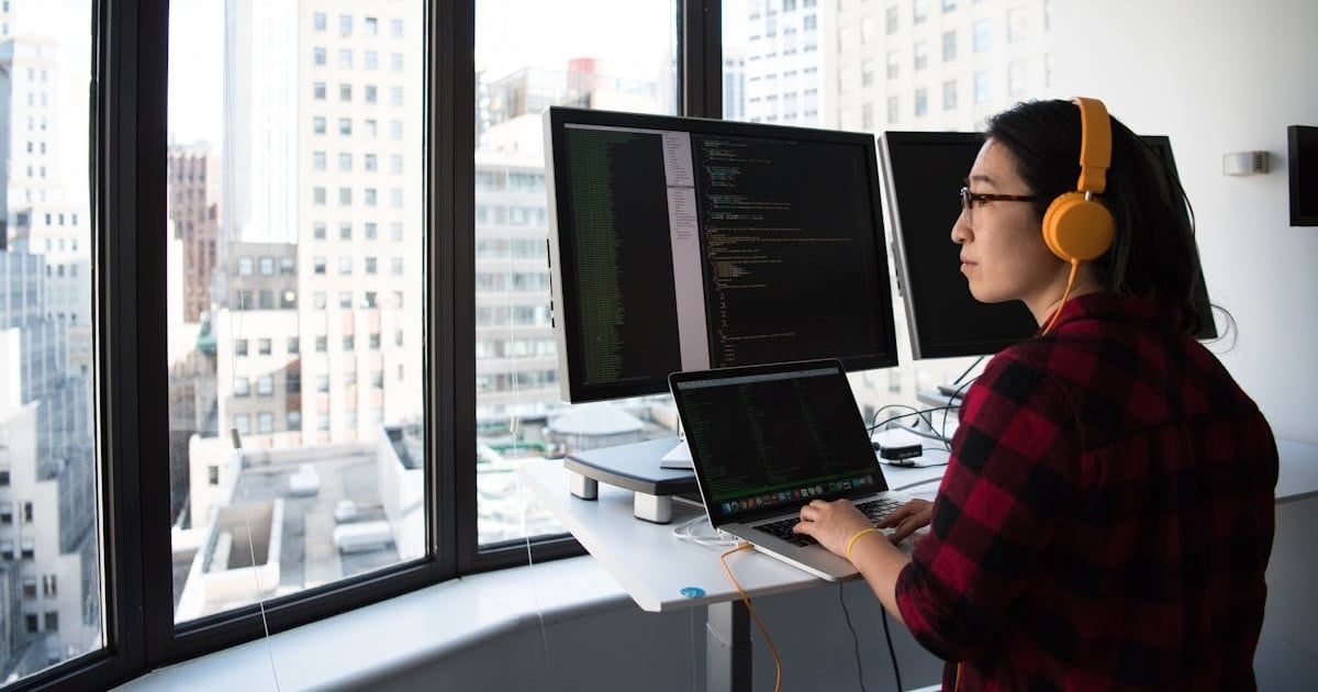 developer looking at a window with laptop and screens with code